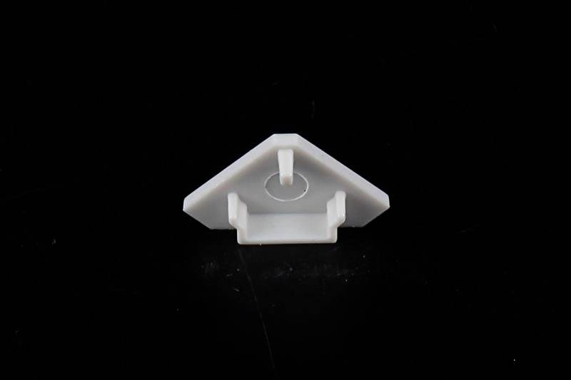 Ein weißes, dreieckiges Kunststoffteil mit einer mittigen Erhöhung, vor schwarzem Hintergrund.