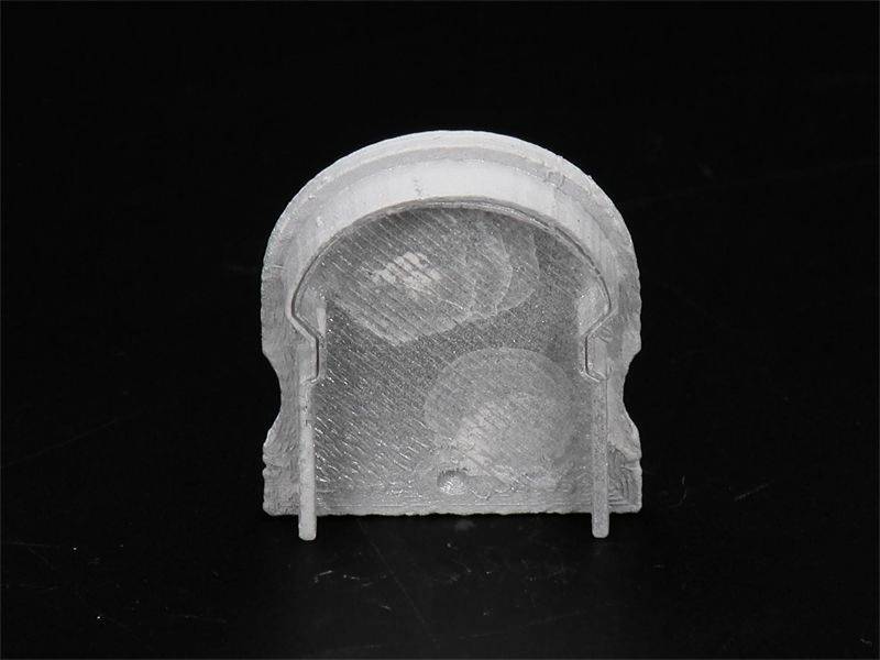 Ein graues Bauteil aus Kunststoff mit bogenförmiger Oberseite und zwei hervorstehenden Füßen auf schwarzem Hintergrund.