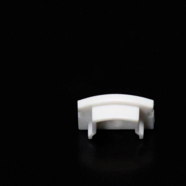 Ein kleines, weißes Plastikobjekt, das an einem dunklen Hintergrund angebracht ist. Es hat eine gebogene Form und scheint Teil eines mechanischen Geräts zu sein.