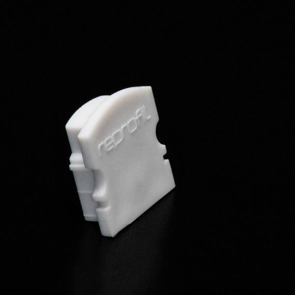 Weiße Kunststoffverbindung auf schwarzem Hintergrund, möglicherweise ein Teil eines Stecksystems oder Kabelverbinders.