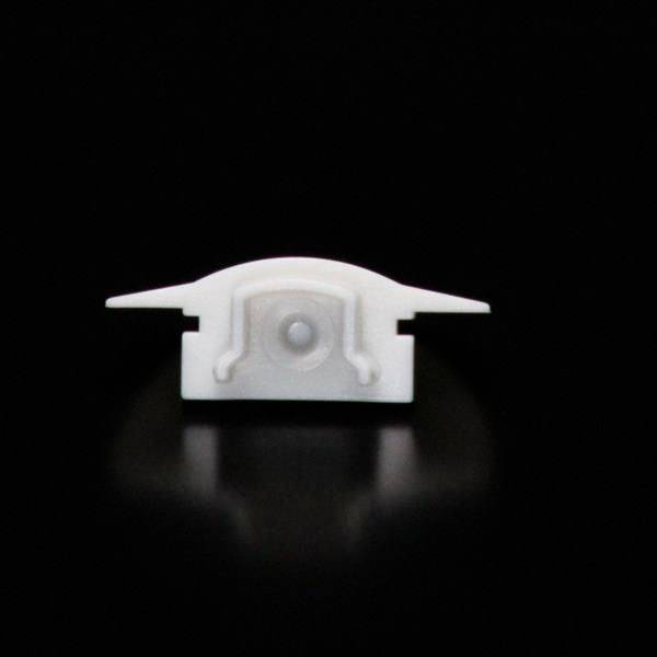Ein weißes Kunststoffteil auf schwarzem Hintergrund, das wie ein kleines, abstraktes Flugzeug aussieht.