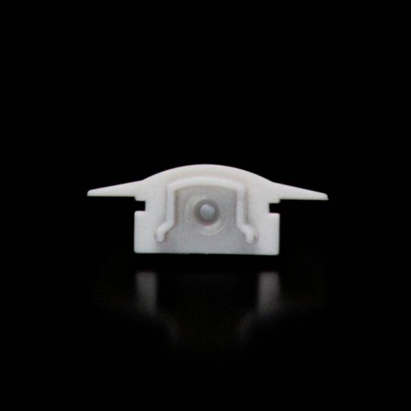 Ein kleiner weißer Gegenstand mit zwei seitlichen Erweiterungen und einer sichtbaren zentralen Erhöhung, platziert vor schwarzem Hintergrund.