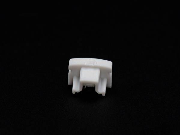 Kleines, weißes Kunststoffteil vor schwarzem Hintergrund.