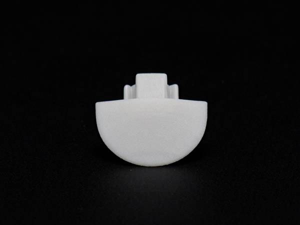 Weiße, halbrunde Kunststoffkomponente vor schwarzem Hintergrund, möglicherweise ein Teil eines mechanischen oder technischen Geräts.