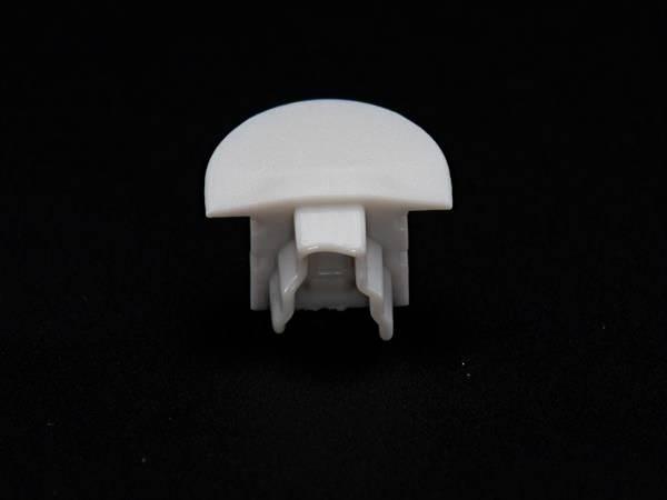 Ein weißes Plastikteil, möglicherweise ein Befestigungs- oder Verbindungselement, auf einem schwarzen Hintergrund.