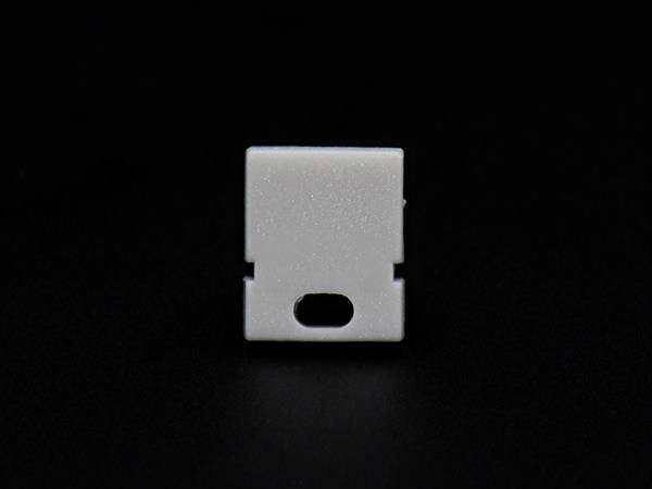 Ein weißes Plastikstück auf schwarzem Hintergrund. Es hat eine rechteckige Form mit einem ovalen Loch unten in der Mitte.