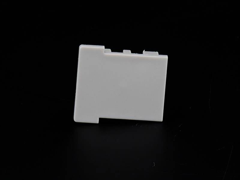 Eine weiße, rechteckige Kunststoffabdeckung vor schwarzem Hintergrund, möglicherweise Teil eines elektronischen Geräts.