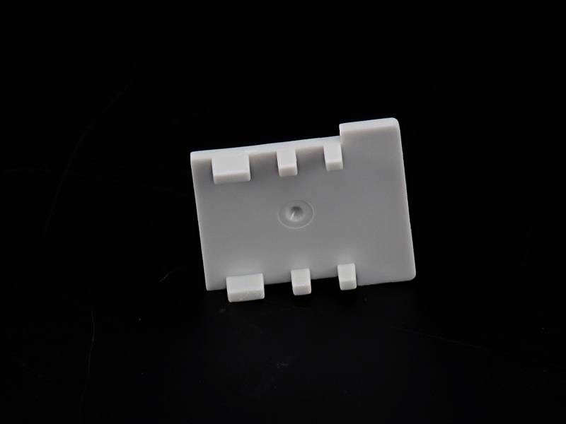 Ein weißes Plastikteil mit mehreren Aussparungen und einem Loch in der Mitte, vor einem schwarzen Hintergrund.