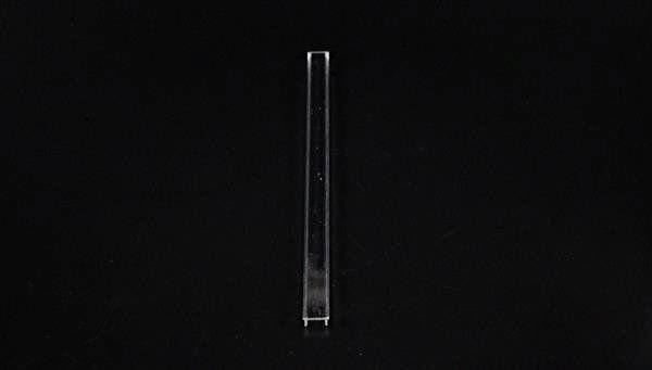 Ein einzelner, durchsichtiger, schmaler Glasstab steht vertikal auf schwarzem Hintergrund.
