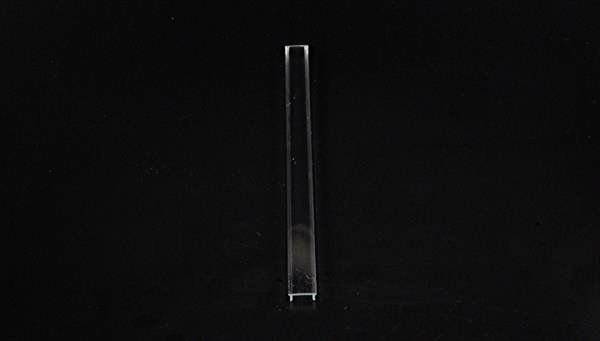 Eine lange, dünne Glasröhre, stehend auf einer dunklen Oberfläche.