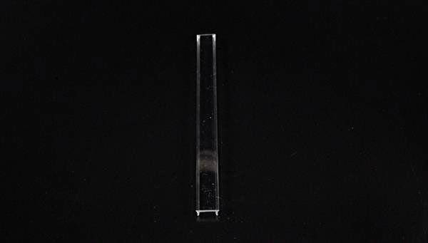 Ein rechteckiges, transparentes Glasobjekt vor schwarzem Hintergrund, vermutlich ein Linsen- oder optisches Element aus Glas.