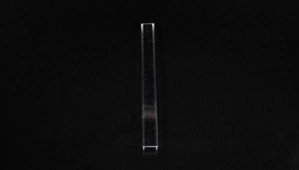Ein schmaler, transparenter Glasstab steht vertikal auf einem schwarzen Hintergrund.