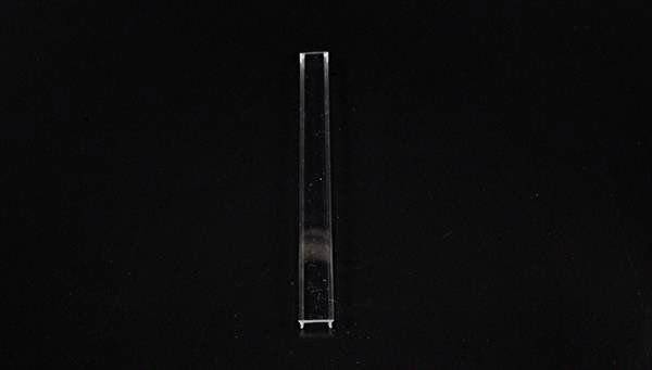 Ein einzelnes, schmales, transparentes Glasobjekt vor schwarzem Hintergrund.