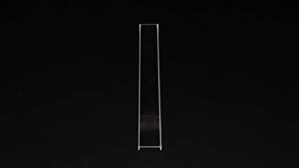 Ein schlichtes, schmales Glasobjekt (Küvette) steht vertikal auf schwarzem Hintergrund. Es wird für Lichtdurchlässigkeitsmessungen verwendet.