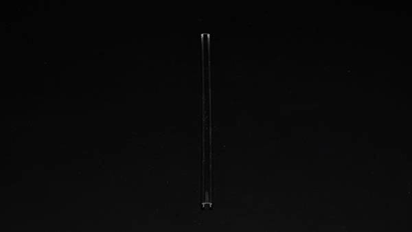 Ein einzelner transparenter Strohhalm vor einem schwarzen Hintergrund, vertikal ausgerichtet in der Bildmitte.