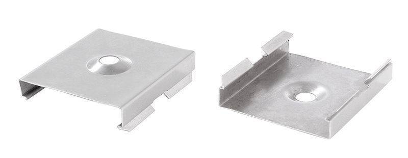 Zwei kleine, metallene Clips nebeneinander mit zentraler Bohrung, jeweils mit gebogenen Enden. Sie dienen zur Befestigung von Materialien.