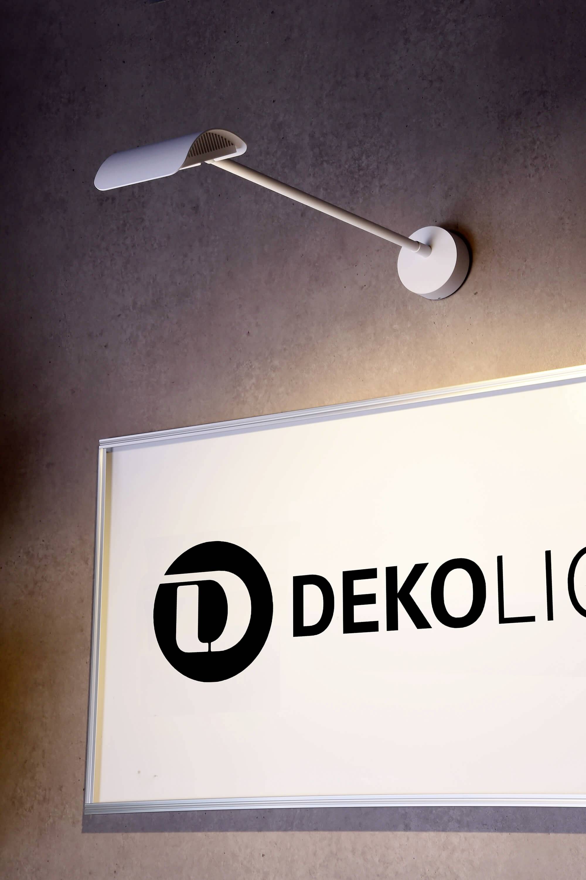 Eine moderne Wandleuchte beleuchtet ein Schild mit der Aufschrift 'DEKOLICHT' in einem minimalistischen, zeitgenössischen Design.