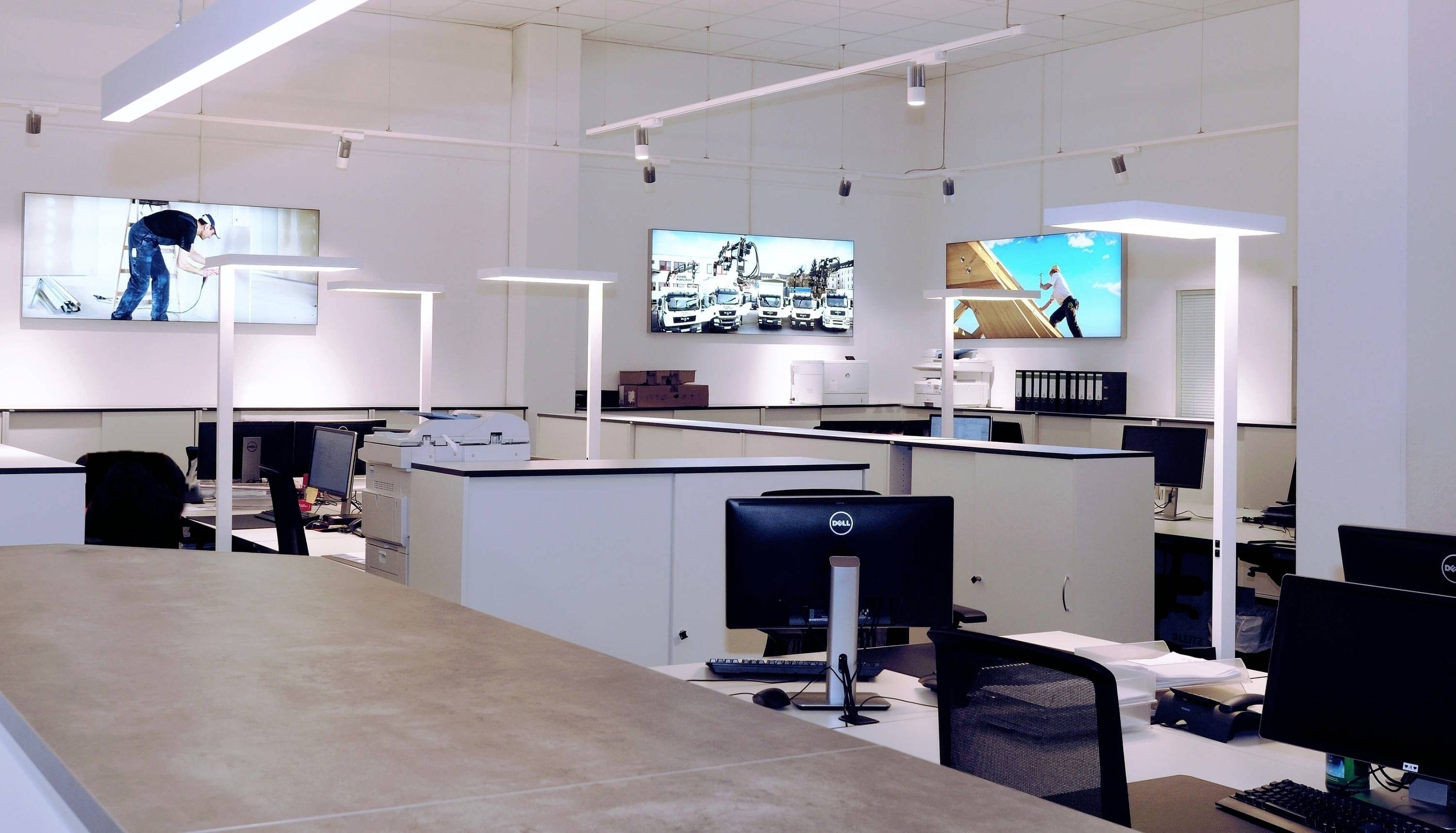 Ein modernes, offenes Büro mit mehreren Arbeitsplätzen und Monitoren an den Wänden, die Bilder von urbanen Szenen zeigen.