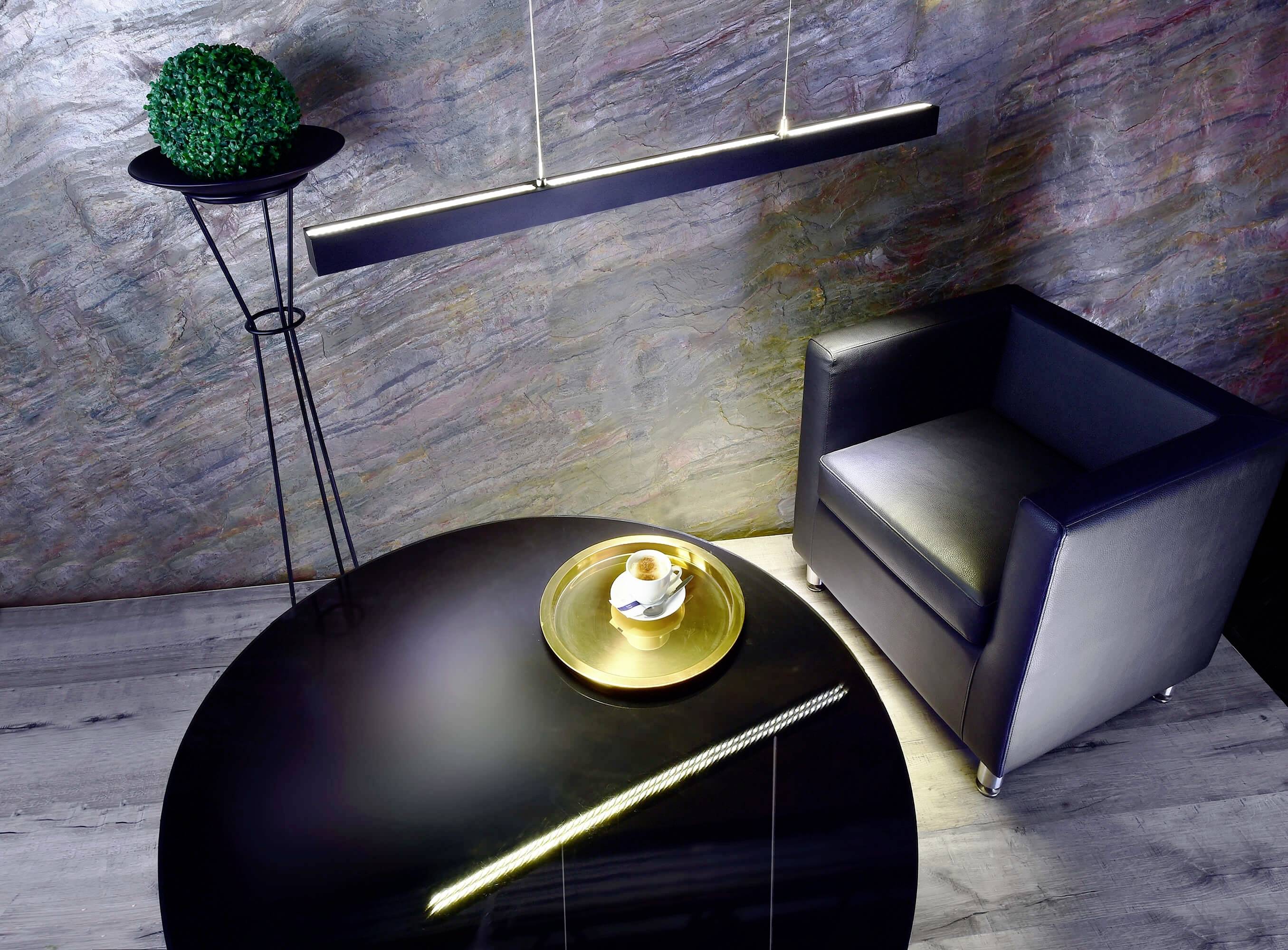 Modern eingerichtet, zeigt das Bild einen schwarzen Tisch mit einer goldenen Platte, auf der eine Tasse steht, daneben ein Ledersessel.
