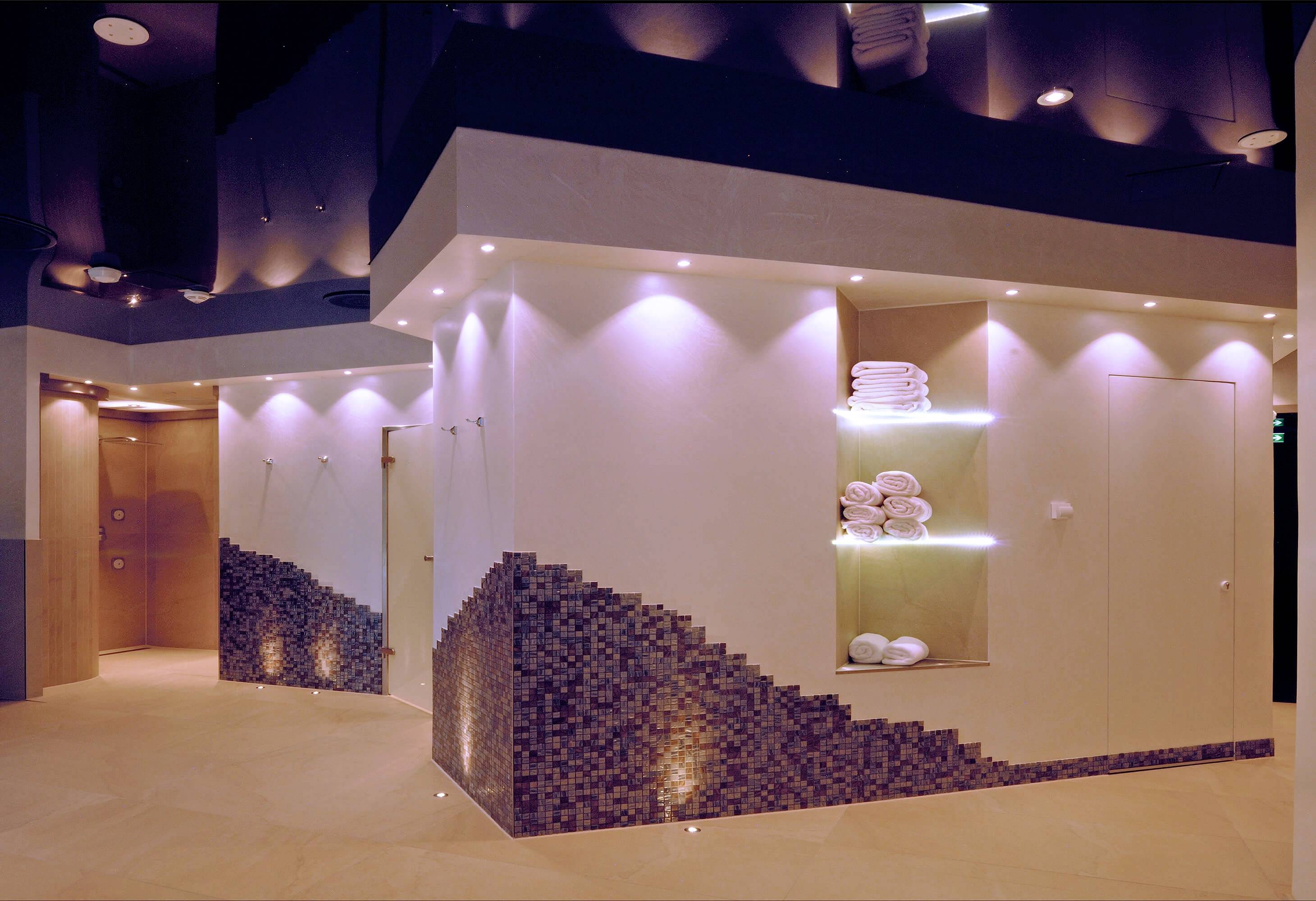Ein moderner, gut beleuchteter Spa-Bereich mit Handtuchregalen und dekorativen Fliesenmustern an den Wänden.