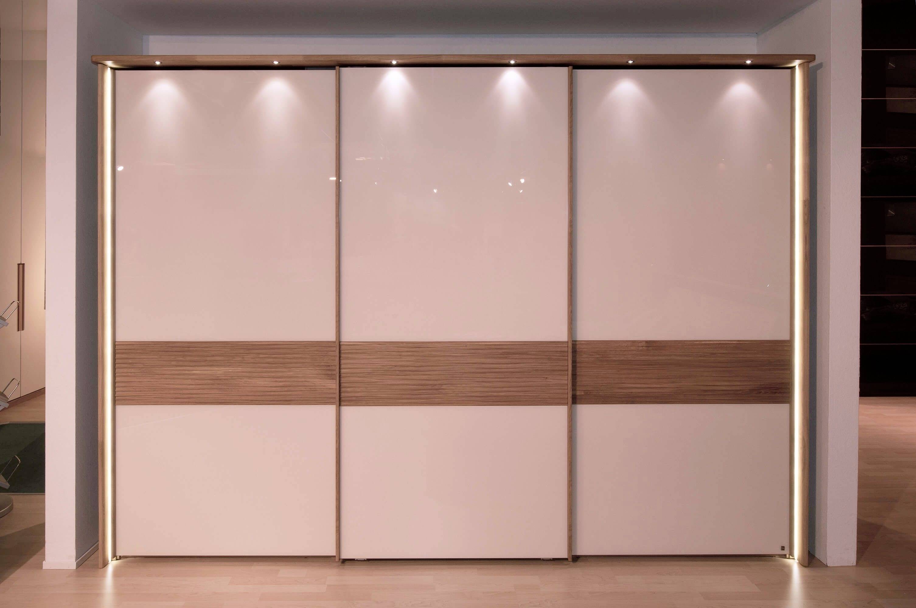 Ein moderner Kleiderschrank mit vier Schiebetüren aus glänzendem Material und Holzdetails; energiesparende LED-Leuchten oben.