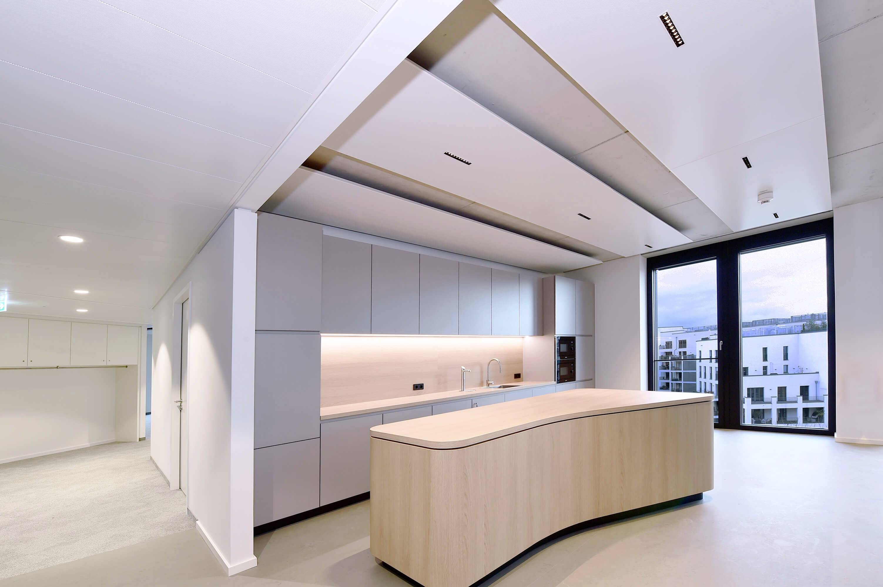 Eine moderne, minimalistische Küche mit geschwungener Holzinsel, eingebautem Herd, weißen Schränken und großem Fenster mit Aussicht.