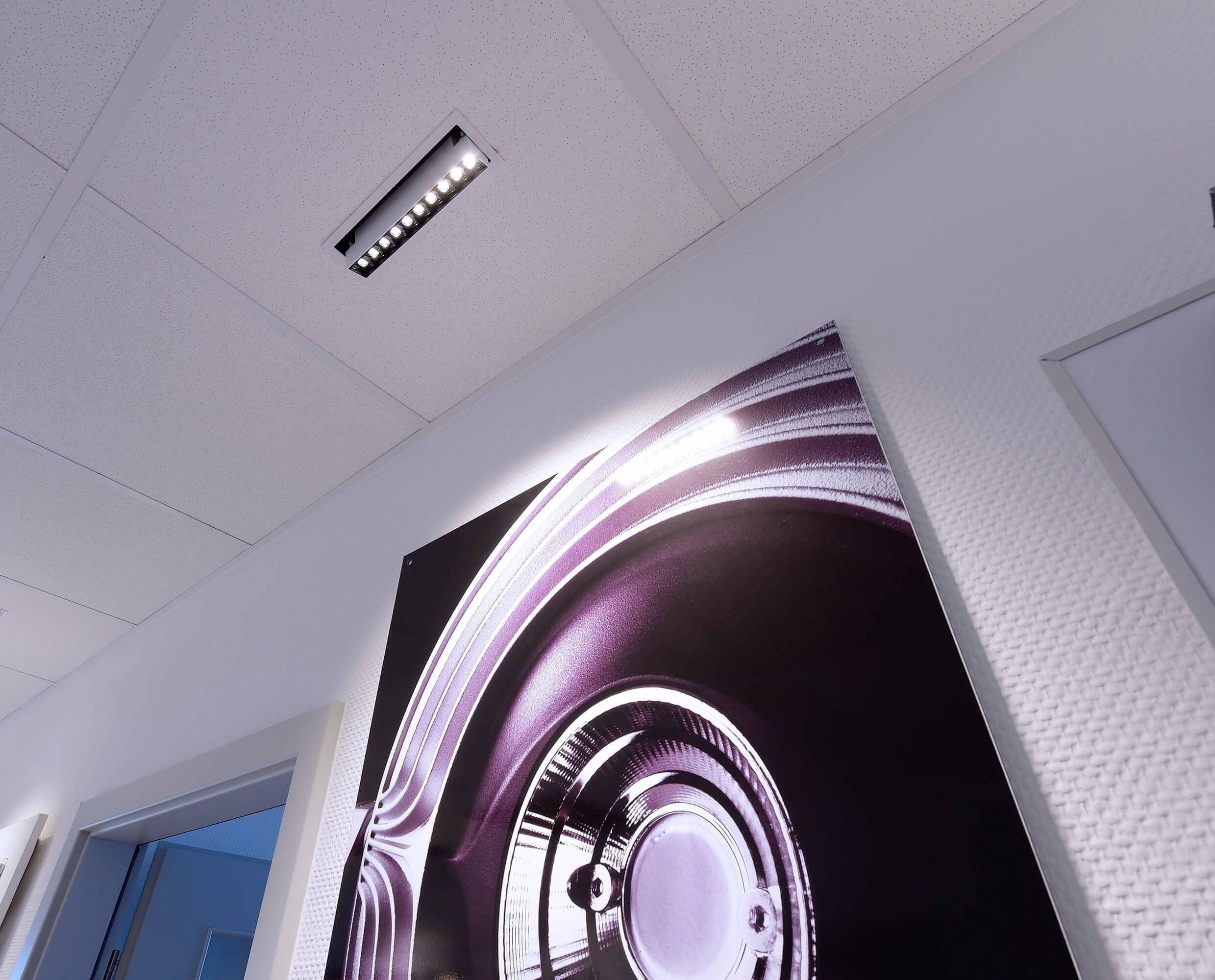 Ein abstraktes Kunstwerk in Lila- und Silbertönen hängt an der Wand eines modernen, hell beleuchteten Raumes.