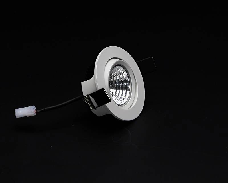 Runde, silberne Einbauleuchte mit stromführendem Kabel auf einem schwarzen Hintergrund.