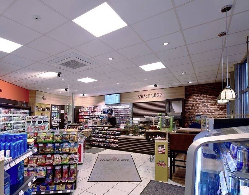 Ein moderner Snack-Shop mit Regalen voller Süßigkeiten und Getränken. Ein Kunde steht an der Kasse, im Hintergrund ein Schild 'Snack Shop'.