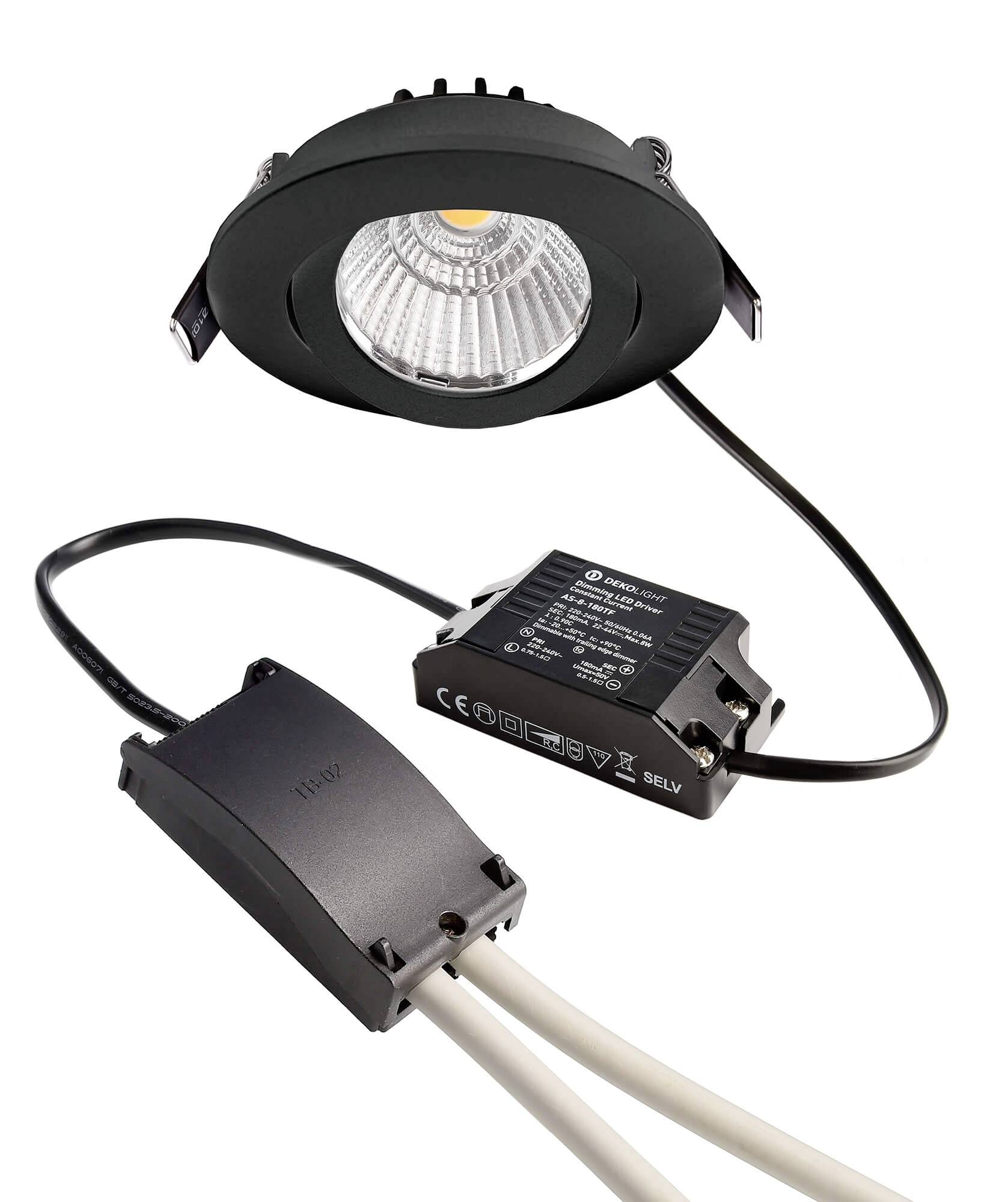 Ein LED-Spotlight für Deckenmontage mit schwarzem Rahmen. Davor liegen ein Transformator und Anschlüsse für Stromversorgung.