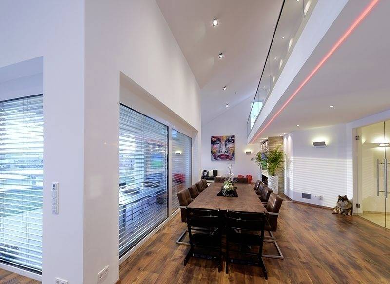 Geräumiges modernes Esszimmer mit langem Holztisch, braunen Ledersesseln, großen Fenstern und Kunstwerken an den Wänden.