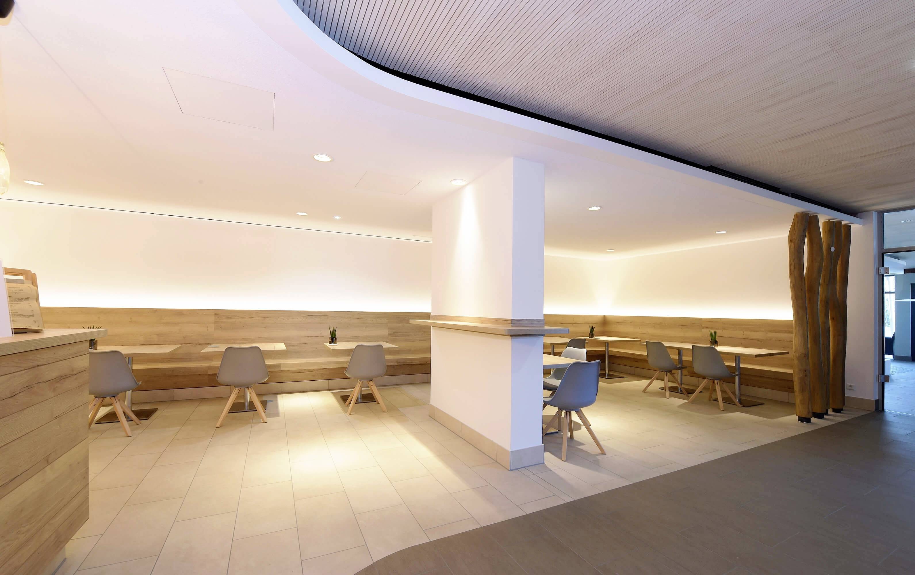 Heller Cafeteria-Raum mit hellen Holzmöbeln, modernen grauen Stühlen und minimalistischer Dekoration.