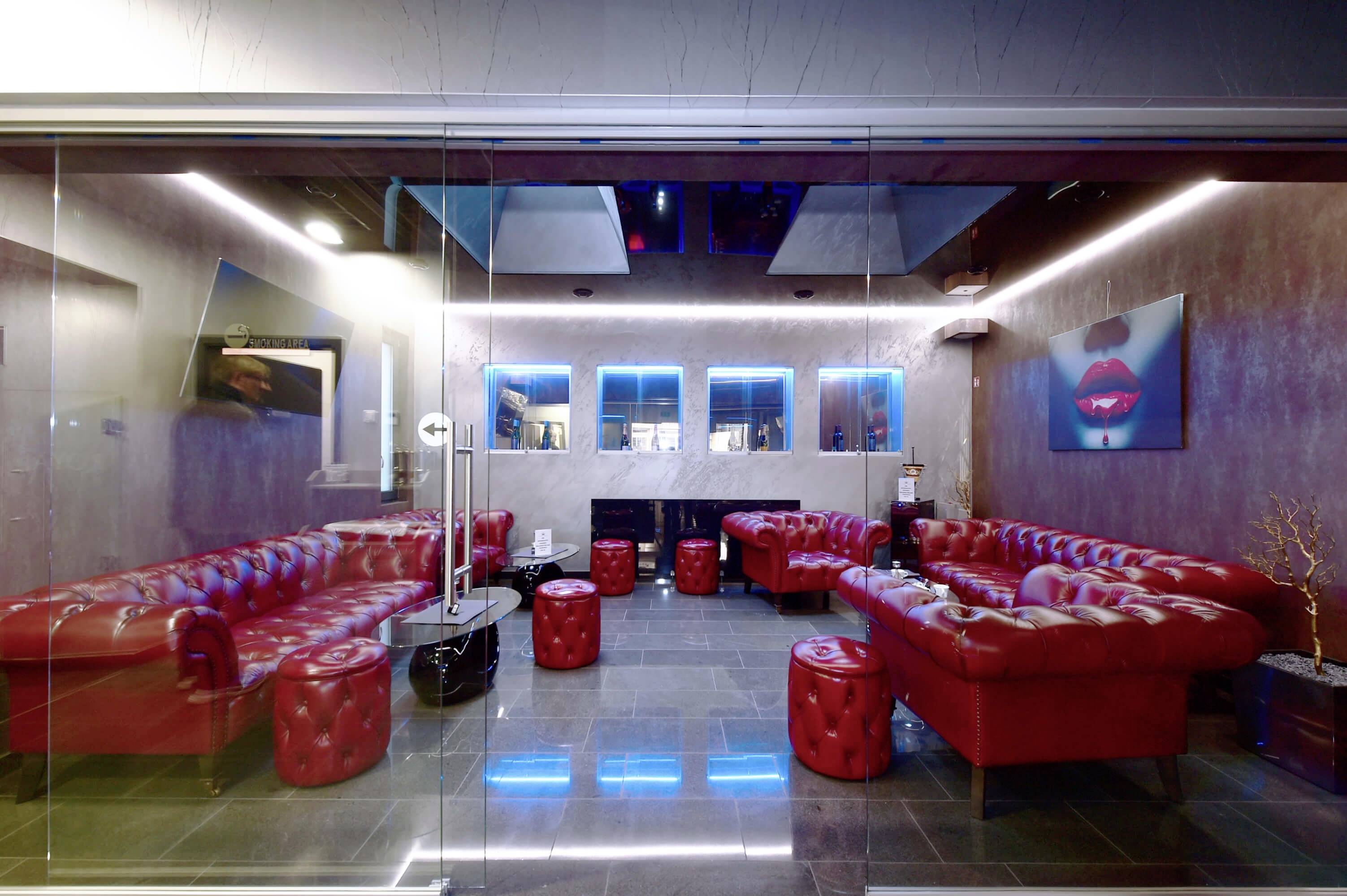 Roter Ledersitzbereich in einer modernen Lounge mit neonblauer Beleuchtung, abstrakten Wandgemälden und Glastisch.