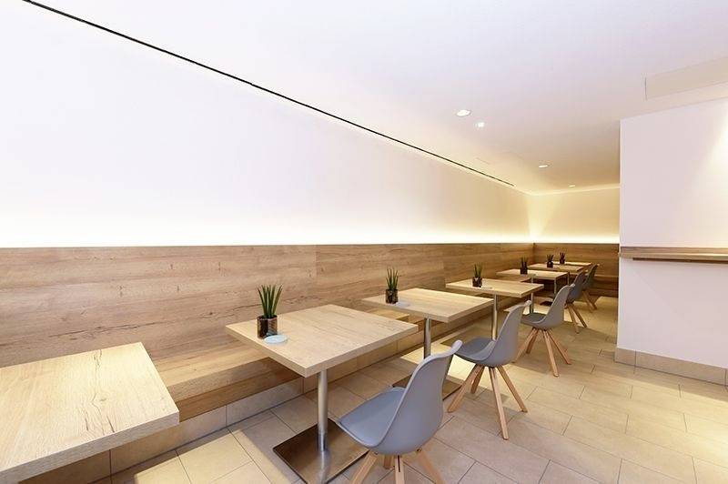 Moderne Cafeteria mit Holztischen und grauen Stühlen, minimalistisches Design. Dezente Beleuchtung und kleine Pflanzen als Dekoration.