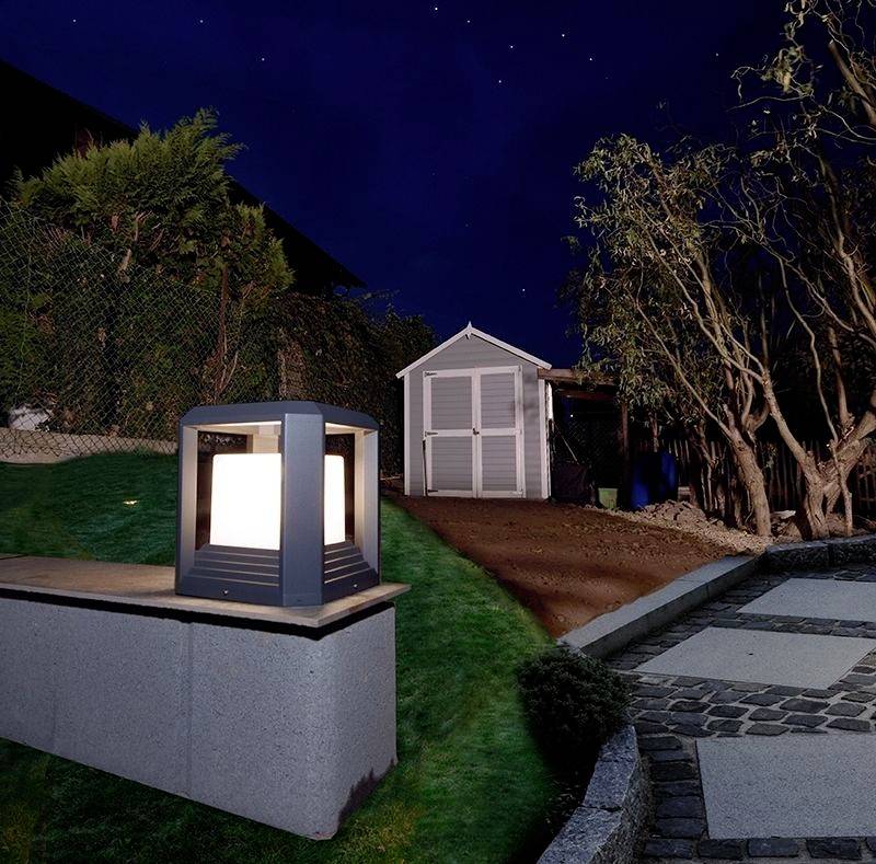 Ein beleuchteter Garten mit Laterne im Vordergrund. Rechts ein gepflasterter Weg. Im Hintergrund ein Schuppen, umgeben von Bäumen bei Nacht.