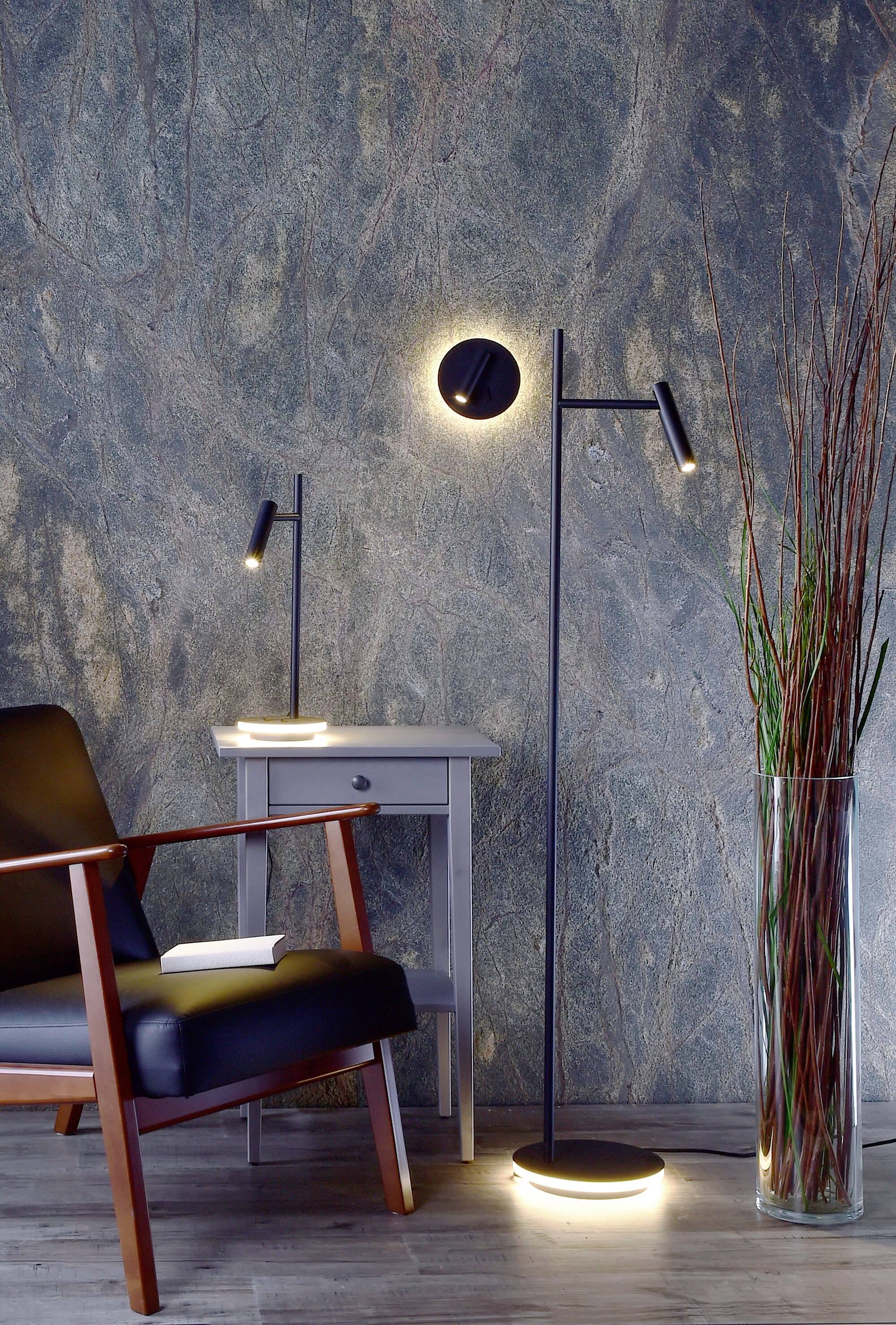 Moderner Wohnbereich mit einem schwarzen Sessel, einem grauen Beistelltisch mit Lampe und einer Stehlampe vor einer strukturierten Wand.