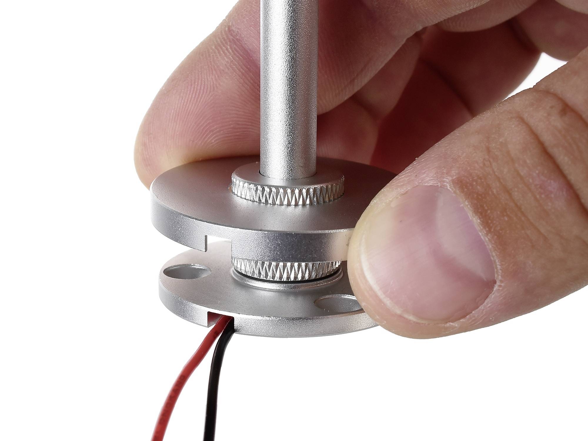 Eine Hand hält ein zylinderförmiges Metallstück mit zwei angeschlossenen Drähten, eines rot, das andere schwarz.