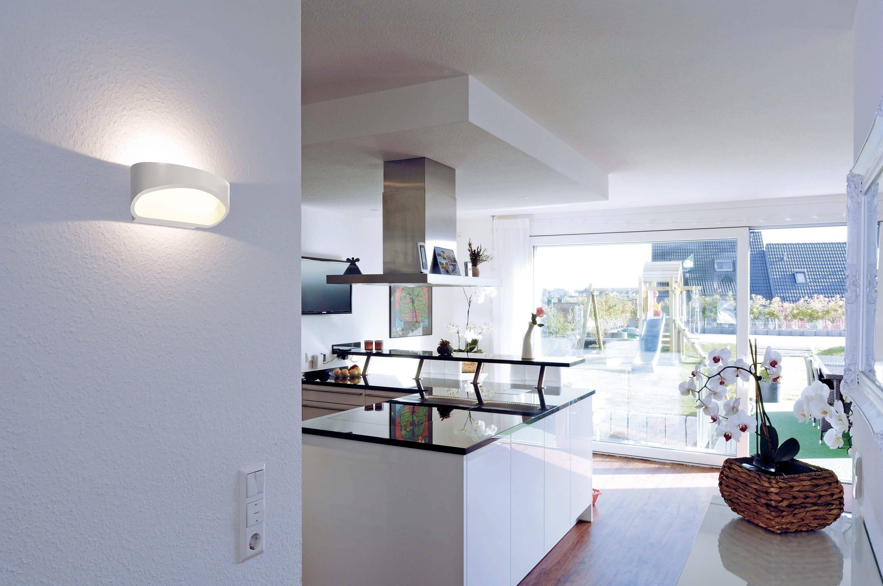 Moderne Küche mit Kochinsel, großen Fenstern und Balkonzugang bei Tageslicht. Orchidee im Vordergrund auf schwarzer Arbeitsplatte.