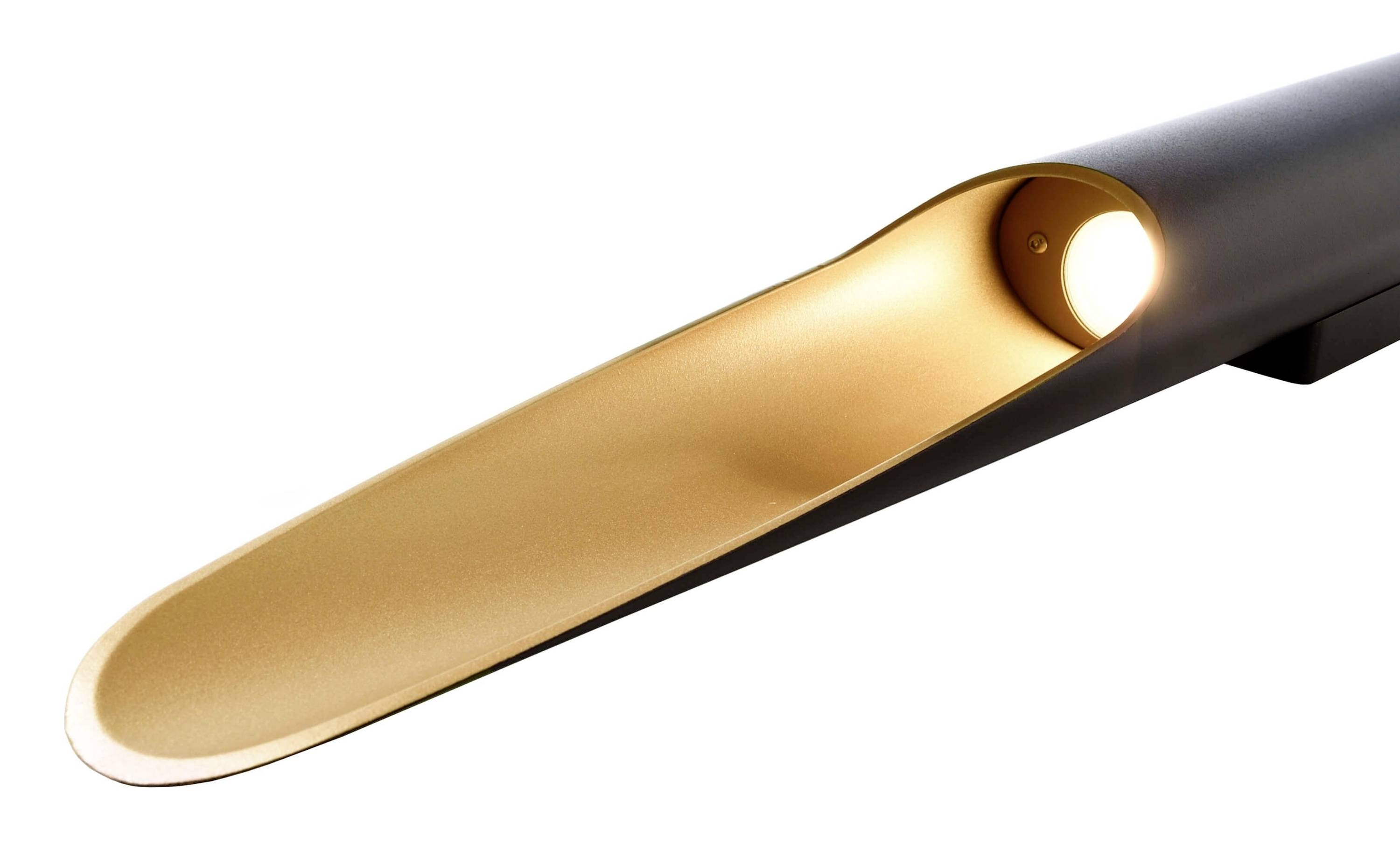 Moderne Lampe mit schlankem, schwarzem Gehäuse und goldfarbenem Inneren, das indirektes Licht aus einer Öffnung abstrahlt.