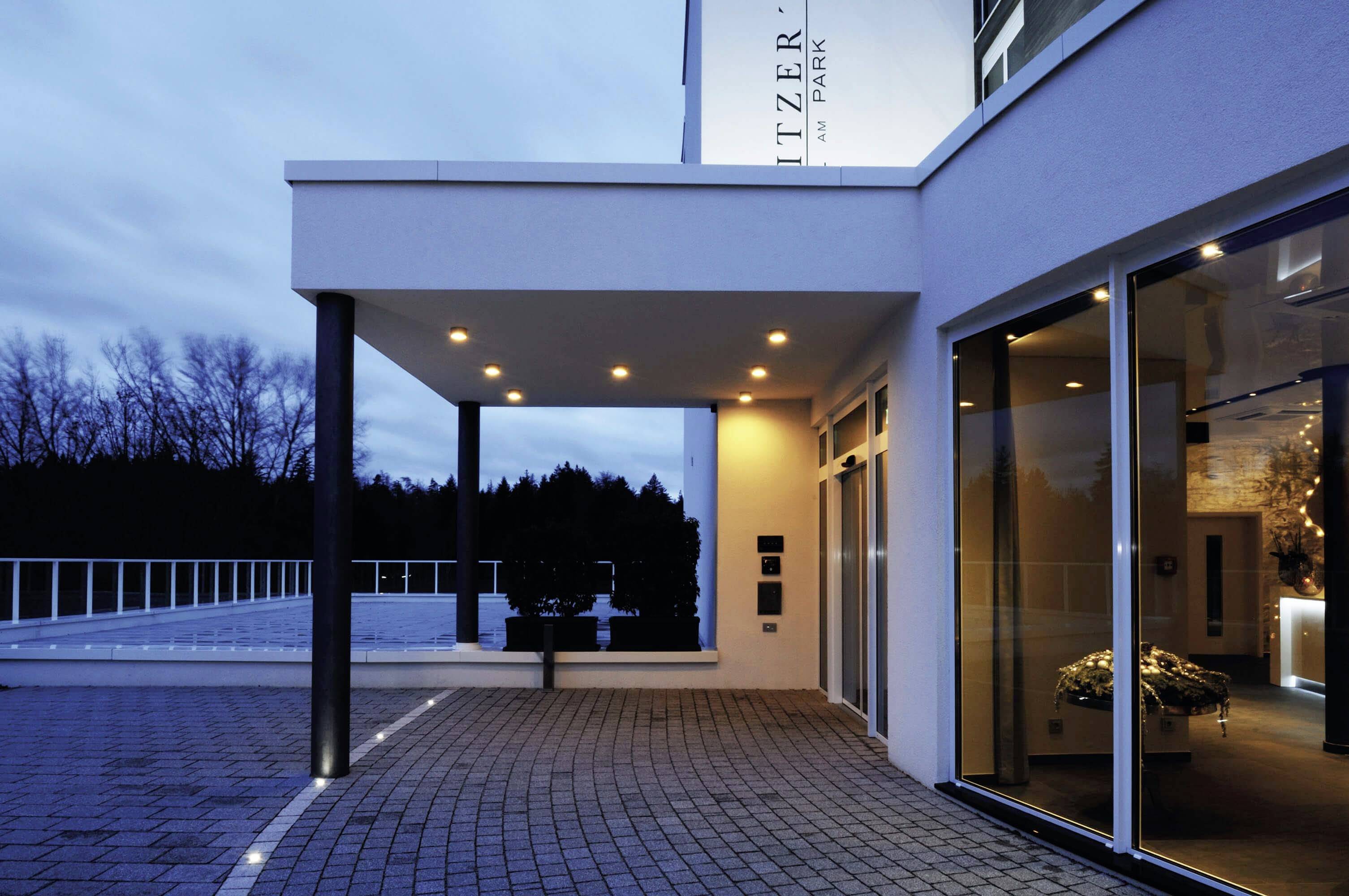 Ein modernes Gebäude bei Dämmerung, beleuchtet mit warmem Licht. Große Fenster zeigen eine einladende Inneneinrichtung.