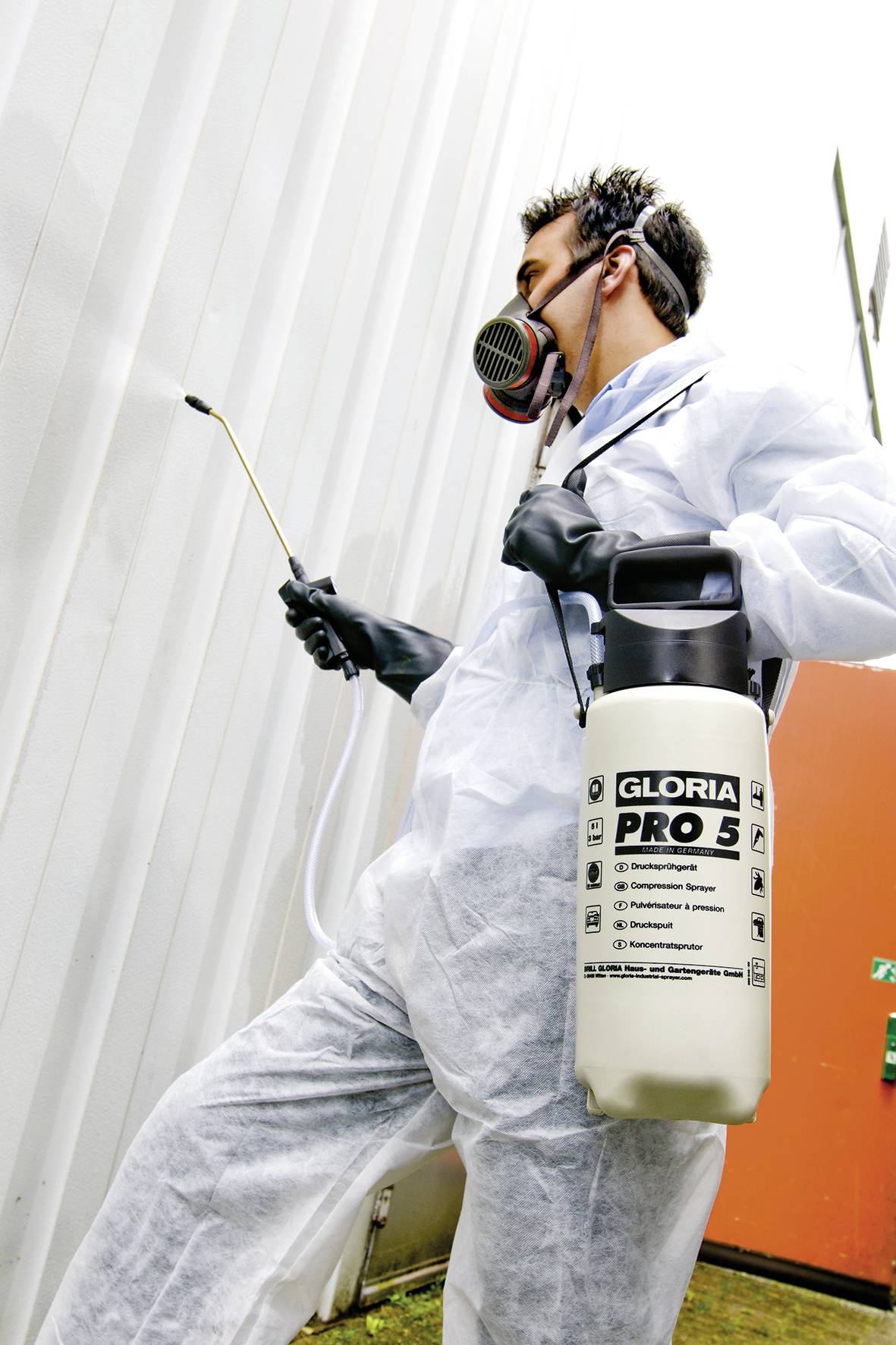 Eine Person in Schutzanzug und Atemmaske sprüht mit einem Drucksprüher eine Wand ein.