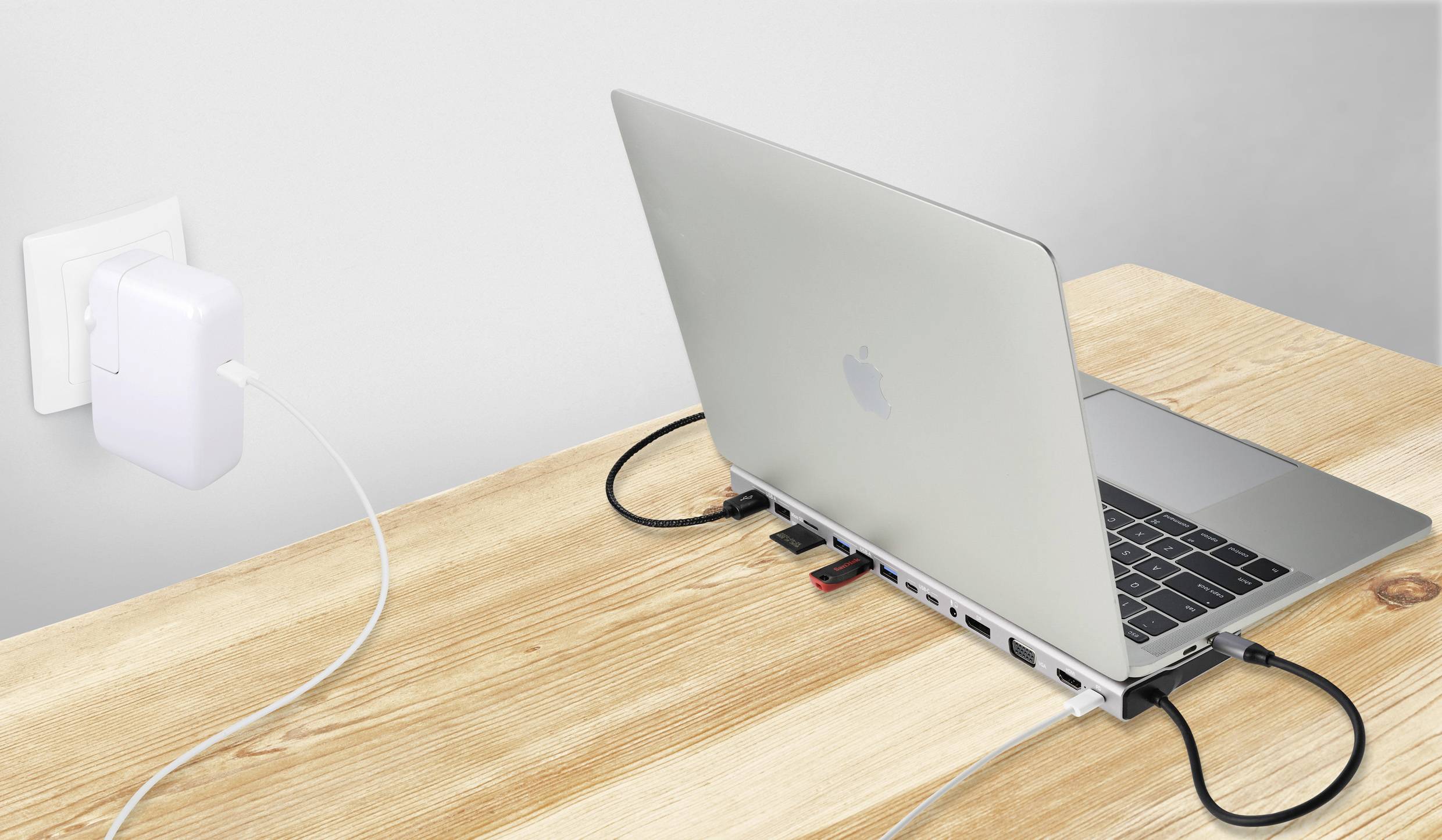 Ein Laptop auf einem Tisch, verbunden mit mehreren Kabeln und einem Ladegerät in einer Steckdose, zeigt eine Arbeitsstation.