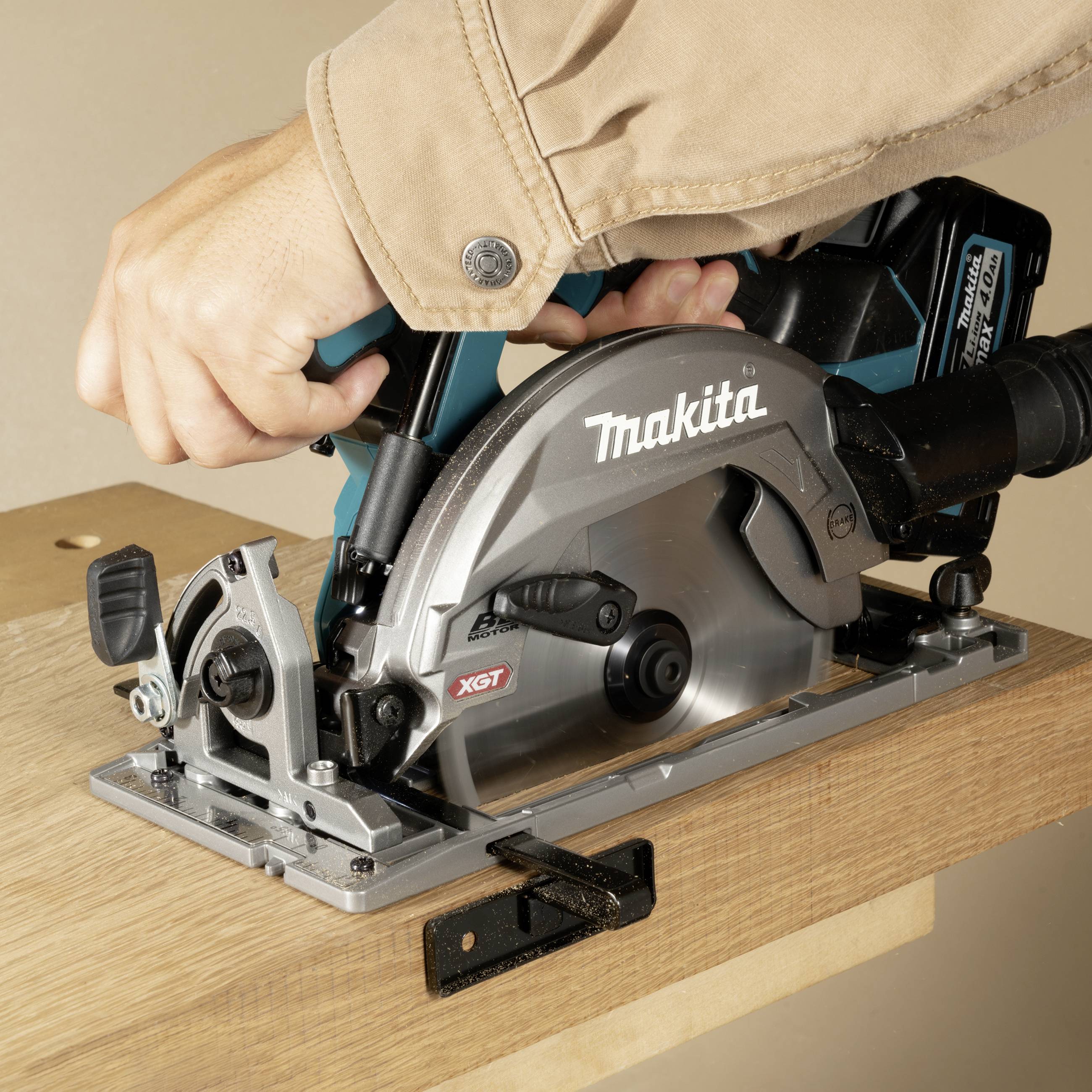 Hand hält eine Kreissäge von Makita, die über ein Holzbrett geführt wird. Die Säge hat eine graue Klinge und ist im Einsatz.