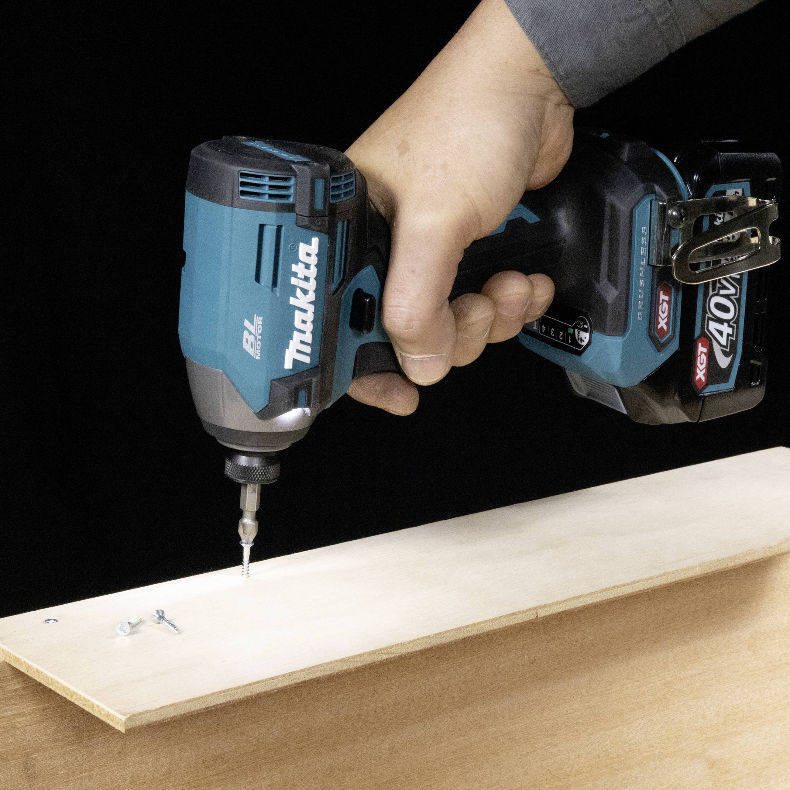 Eine Hand hält einen elektrischen Schraubendreher und zieht eine Schraube in ein Holzbrett ein. Markenname 'Makita' sichtbar.
