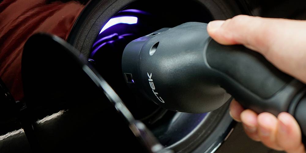 Eine Hand steckt ein Ladekabel in die Ladebuchse eines Autos ein.