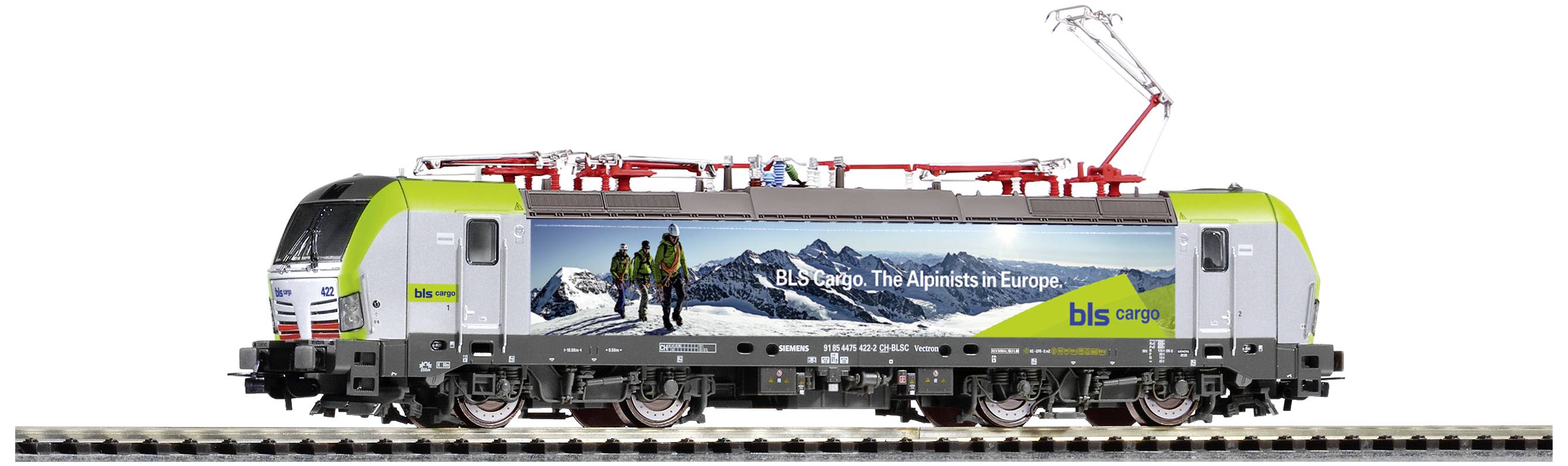 Eine grüne Lokomotive mit Werbung 'BLS Cargo. The Alps–in Europe' fährt auf Schienen. Sie hat ein Bild von Bergen und Wanderern.
