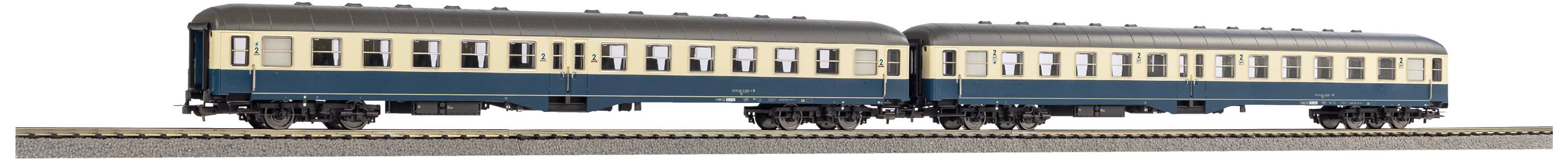 Zwei blaue und beige Modellbahnwaggons stehen auf Schienen, repräsentieren historische Zugmodelle.