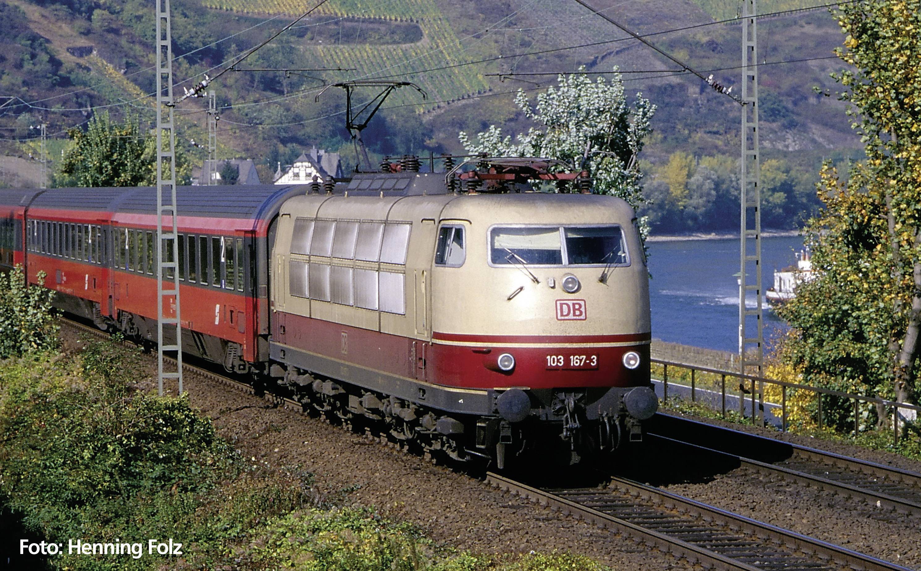 Zug der Deutschen Bahn fährt durch eine landschaftlich reizvolle Gegend am Fluss entlang. Bäume und Weinberge sind im Hintergrund zu sehen.