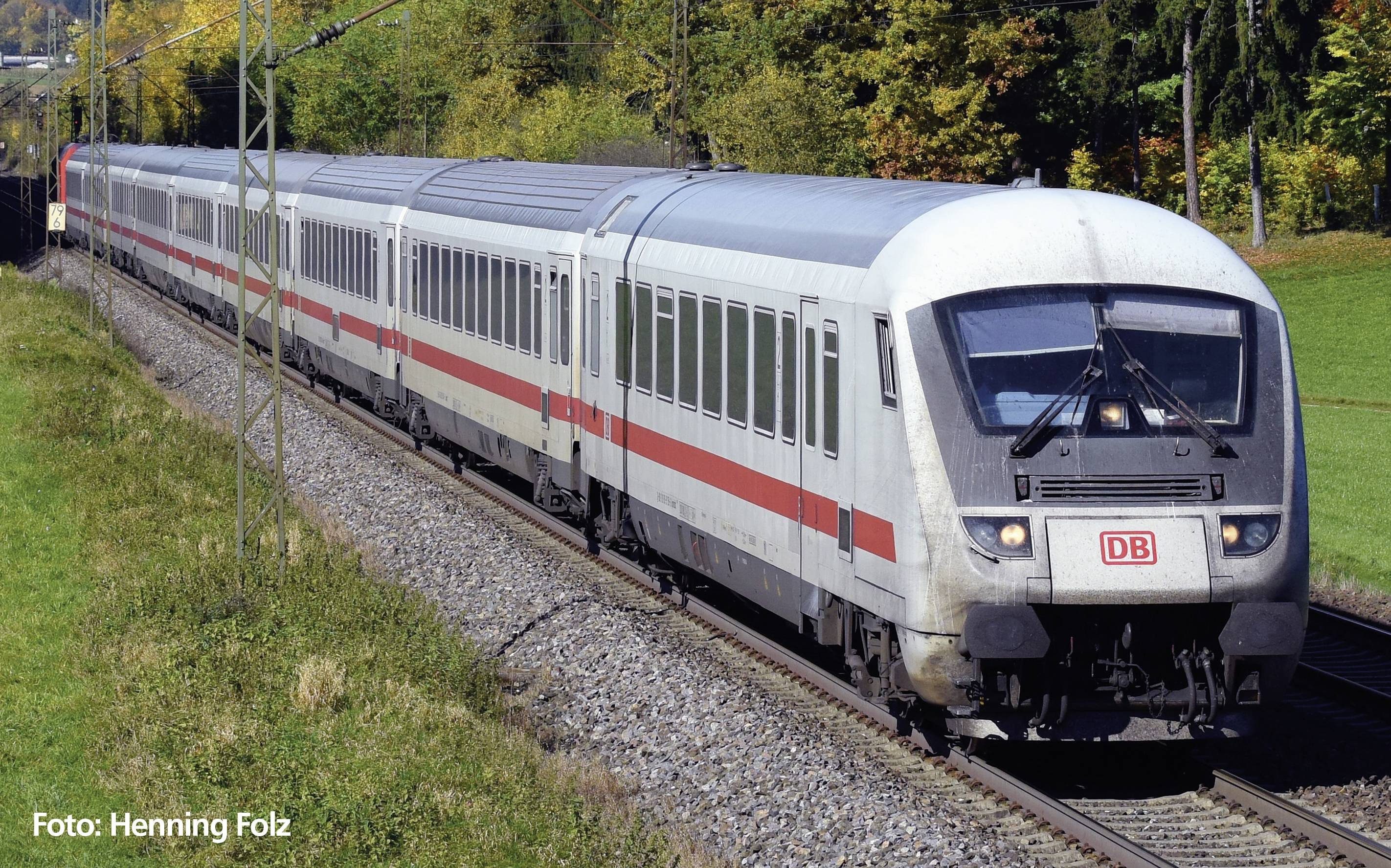 Ein Zug der Deutschen Bahn fährt auf einer ländlichen Bahnstrecke, umgeben von herbstlichen Bäumen und grünen Feldern.