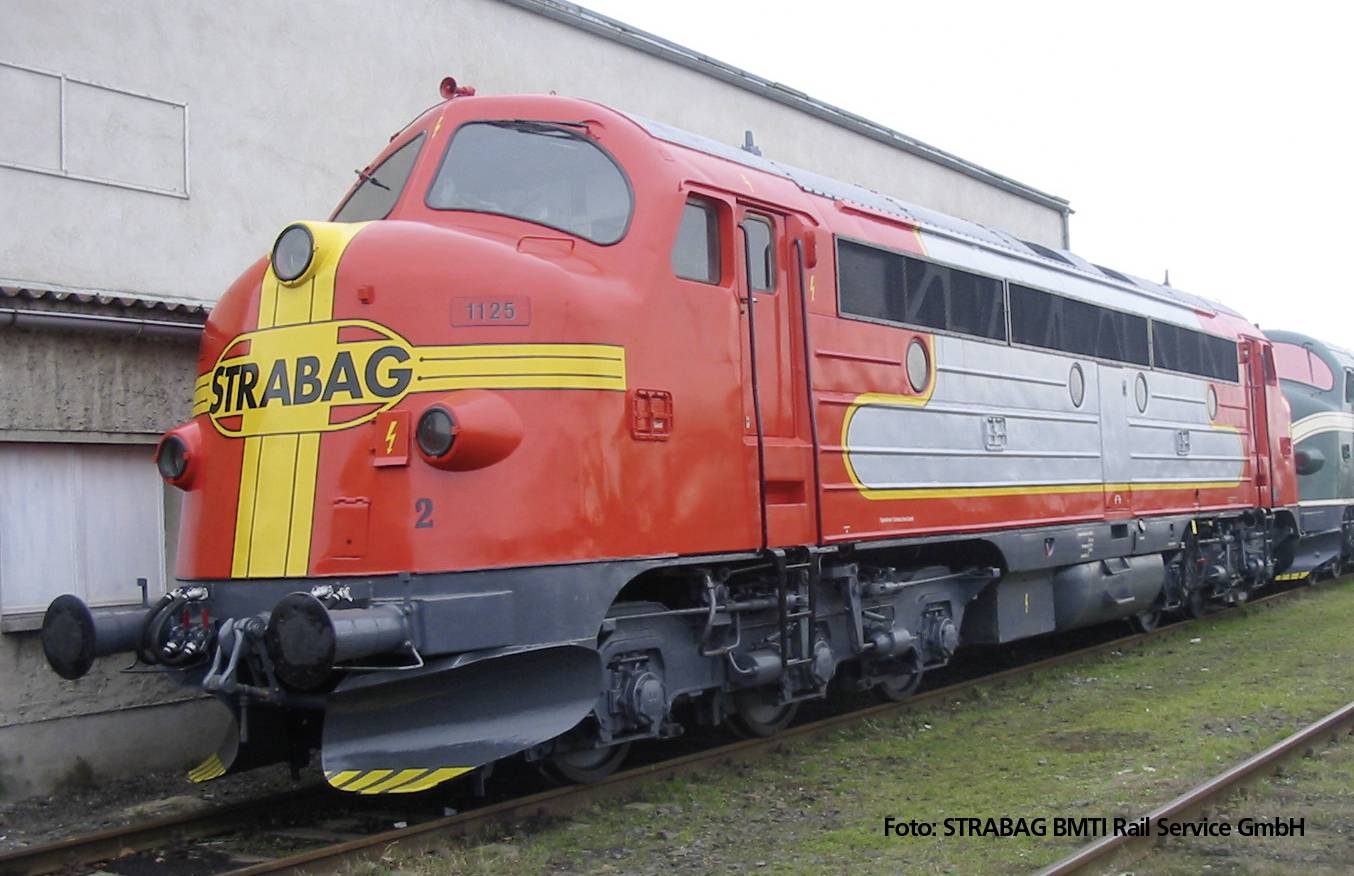 Eine rote Diesellok mit der Aufschrift 'STRABAG' steht auf einem Abstellgleis. Die Lok trägt gelbe und silberne Streifen.